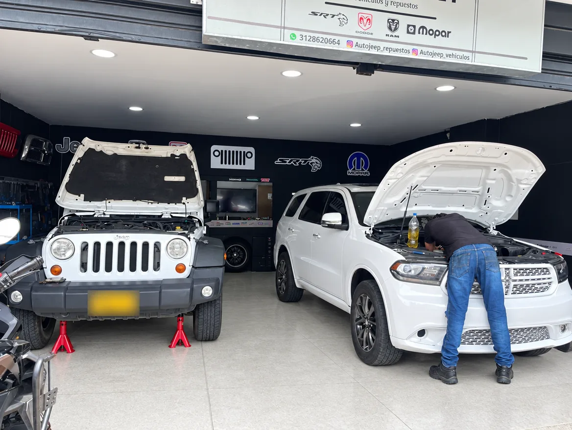 Mecánico de AutoJeep trabajando en el motor de una Dodge Durango junto a un Jeep Wrangler